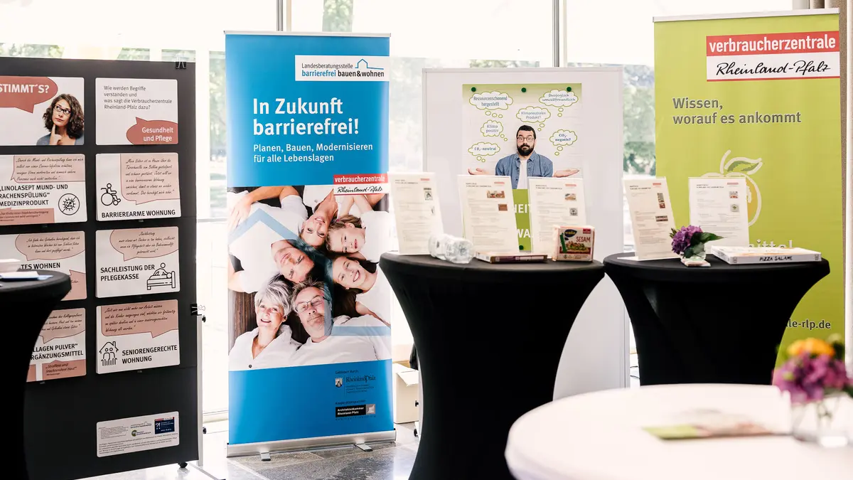 Ein Messestand mit zwei Stehtischen und Plakaten im Hintergrund.