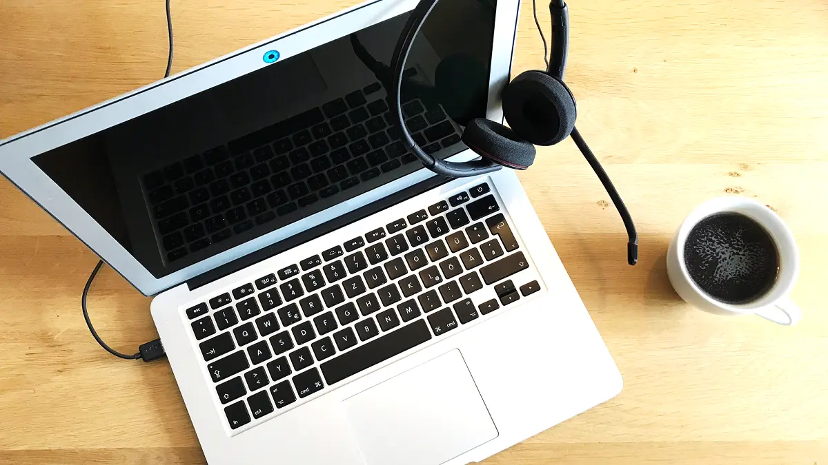 Ein Laptop mit Kopfhörern und eine Kaffeetasse stehen auf einem Tisch.