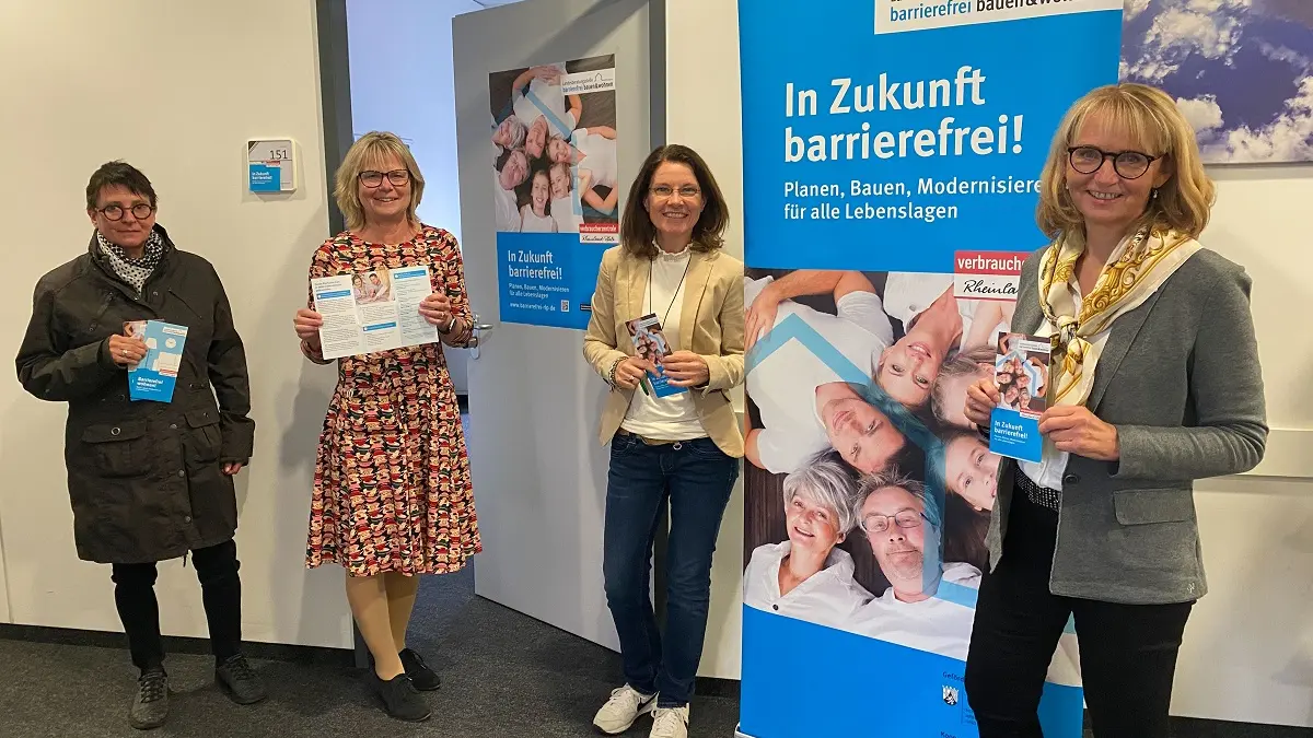 Vier Frauen stehen vor einem Plakat und lachen in die Kamera. Der Anlass ist die Wiedereröffnung der Landesberatungsstelle in Ingelheim