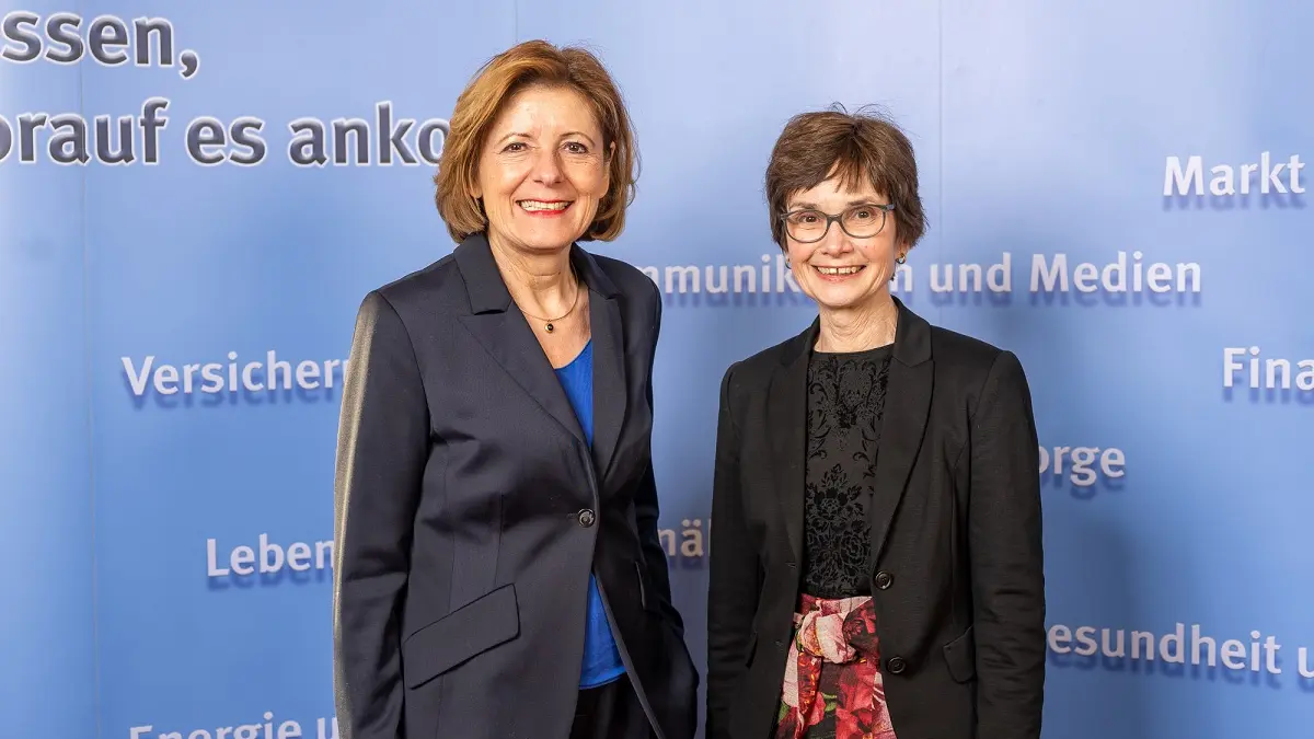Zwei Frauen stehen vor einer blauen Wand und Blicken in die Kamera