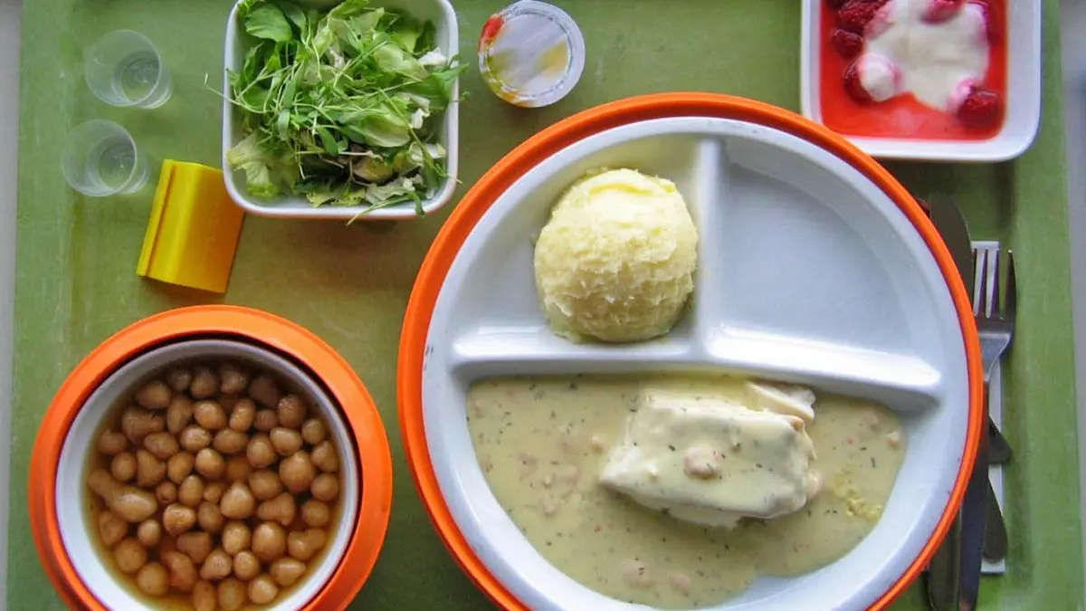 Ein Krankenhaustablett mit verschiedenen, portionierten Essensgängen drauf und zwei Gläsern Wasser.