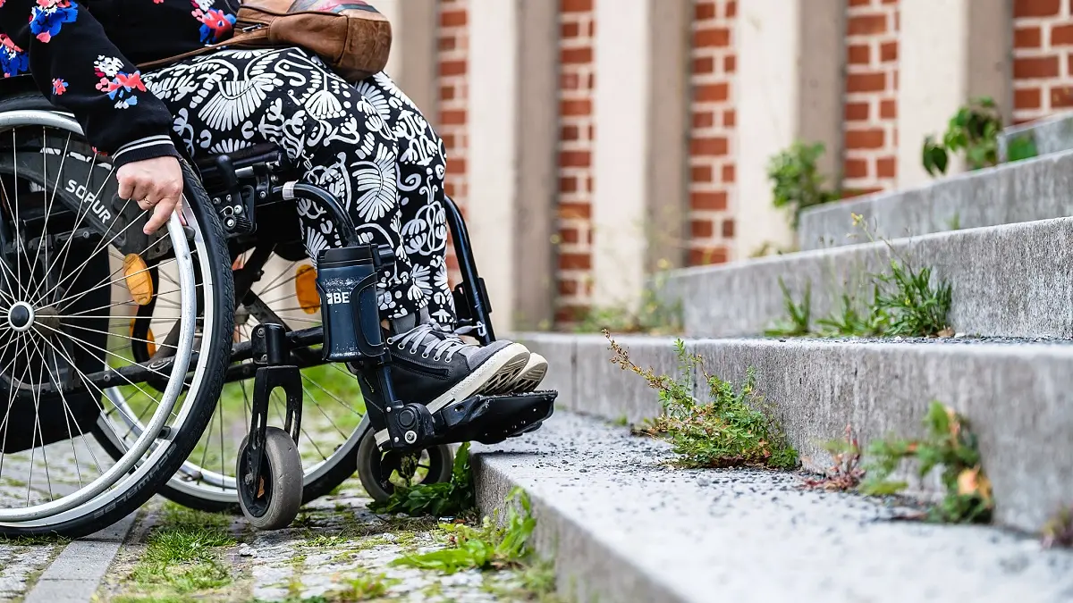 Eine Person im Rollstuhl steht vor einer Treppe und kann nicht weiter fahren.