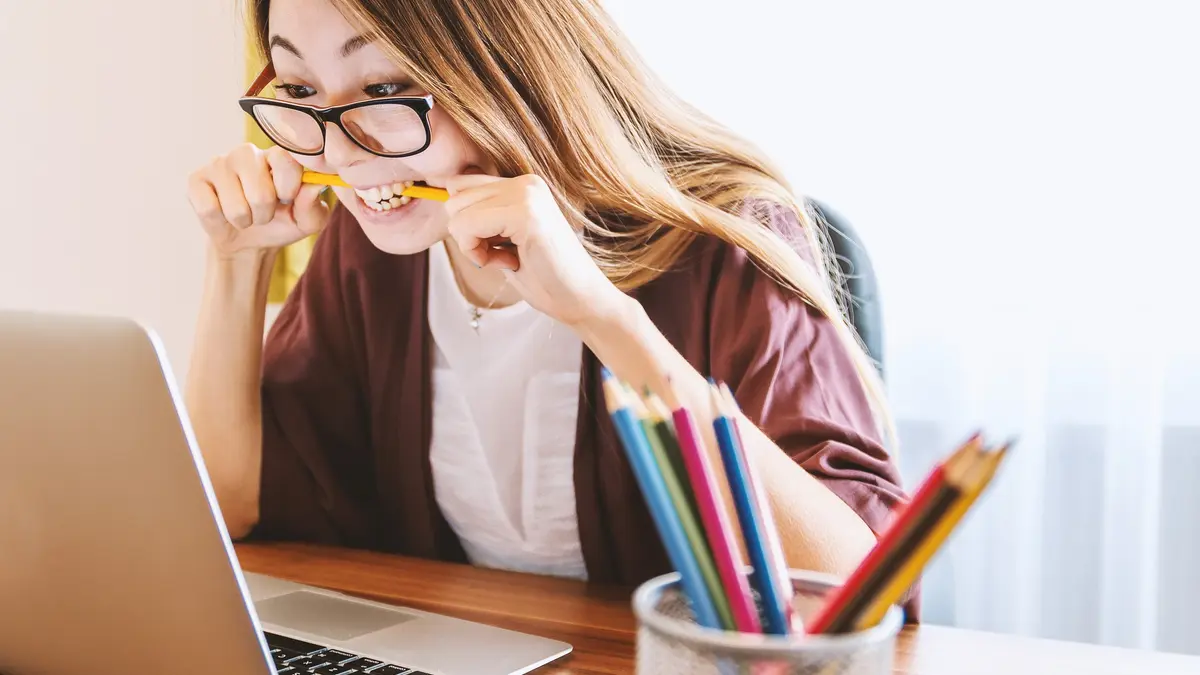 Eine Frau sitzt vor dem Laptop und beißt verzweifelt auf einen Bleistift.