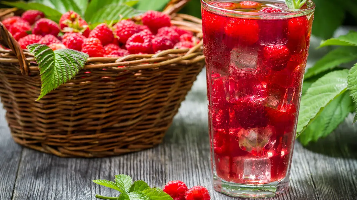 Neben einem Korb mit Himbeeren steht ein Glas mit Himbeer-Shrub