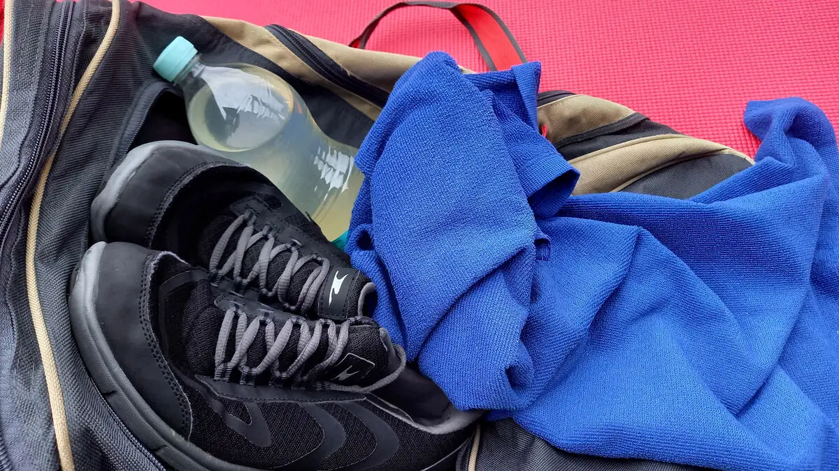 Eine Flasche mit einem Sportgetränk liegt auf einer Trainingstasche, daneben Turnschuhe und ein Handtuch