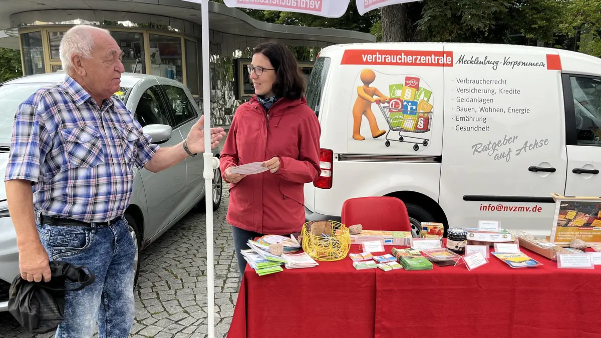 zwei unterhaltende Menschen vor dem Verbraucherzentralen Auto