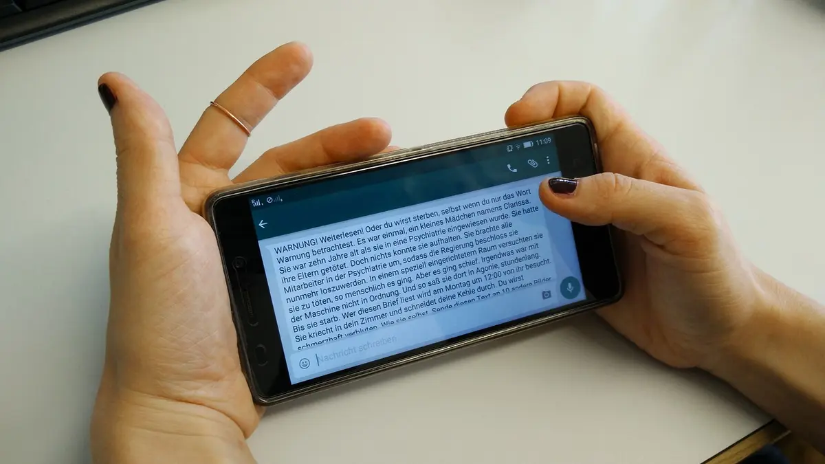 Eine Frau hält ein Handy in der Hand uns liest einen Kettenbrief.
