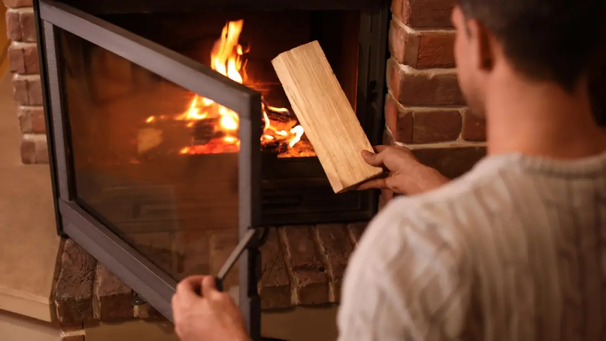 Ein Mann legt einen Holzscheit in einen Kamin.