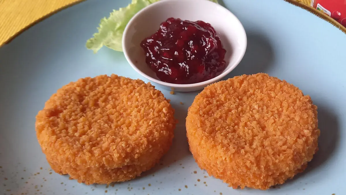 Zwei Scheiben gebackener Camenbert und eine kleine Schüssel mit Preiselbeeren auf einem Teller.
