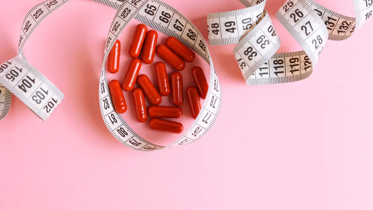 Rote Abnehmtabletten liegen auf einem Tisch, umschlossen von einem Maßband