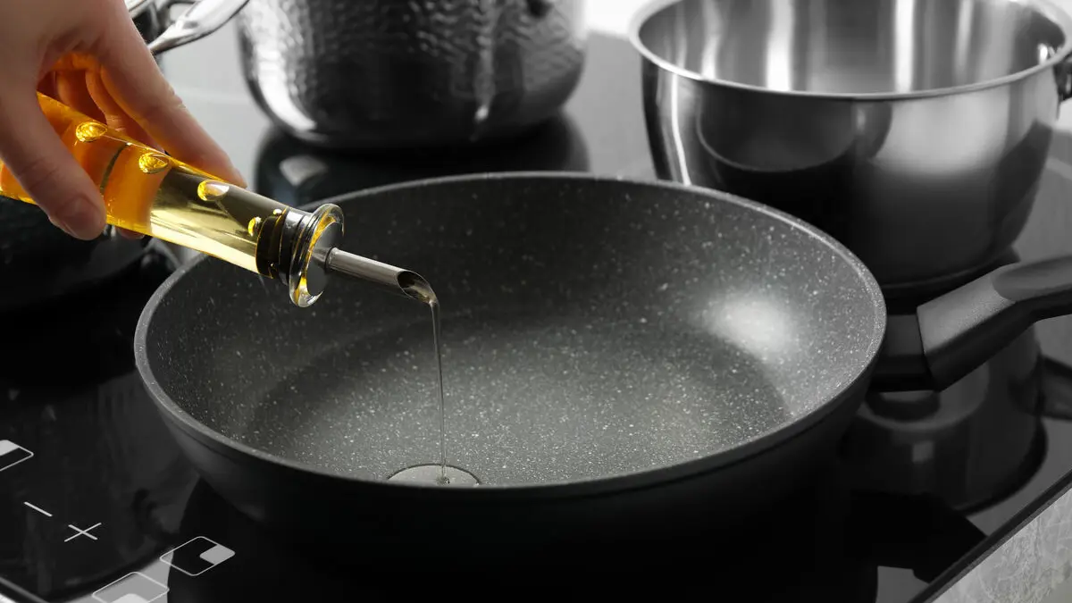 Öl aus einer Glasflasche wird in eine Pfanne geschüttet.