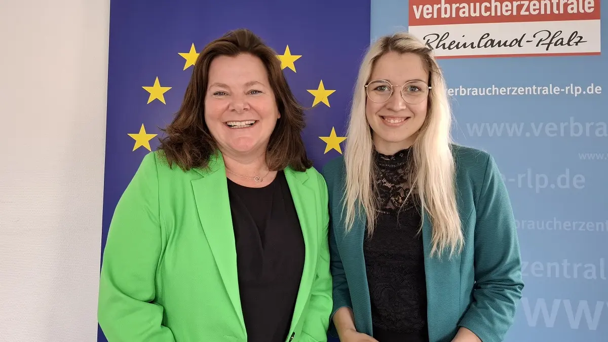 Zwei Frauen vor einem Banner mit der Europa-Flagge und lächeln in die Kamera.