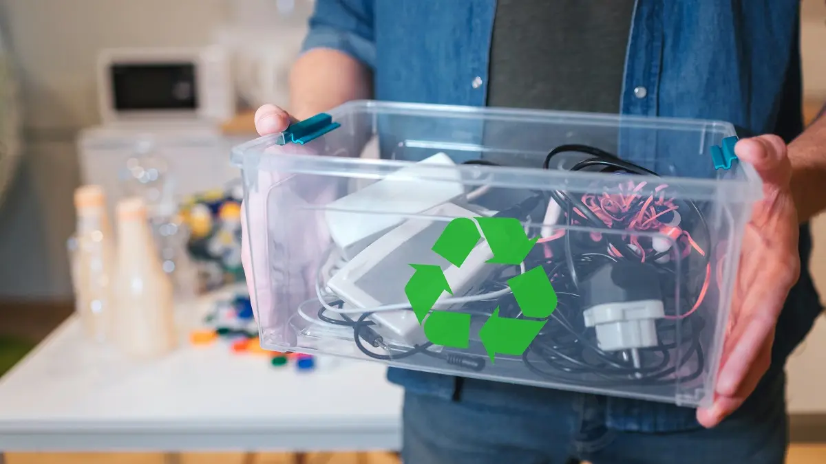 Ein Mann hält eine Plastikkiste in den Händen, die mit Elektro-Schrott gefüllt ist.