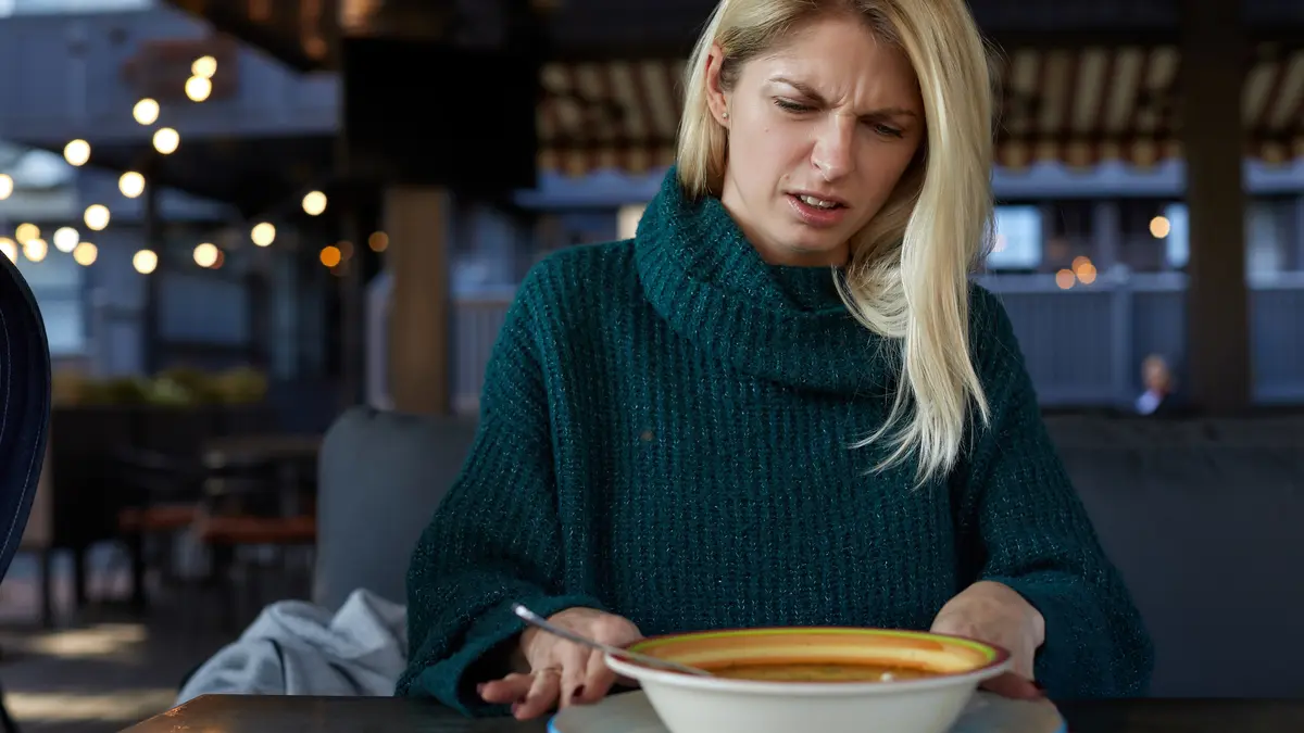 Eine Frau schaut angeekelt auf einen Teller mit offenbar verdorbenem Essen.