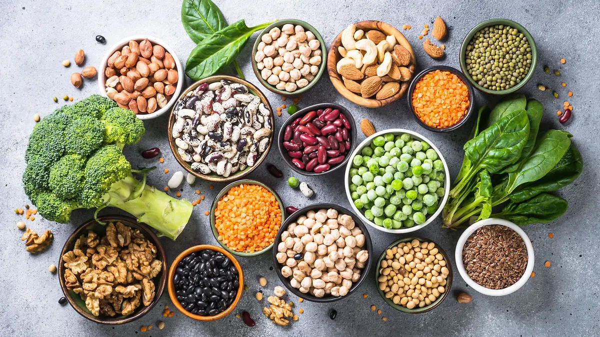 Verschiedene vegane eiweißreiche Lebensmittel, wie etwas Linsen, Bohnen oder Nüsse, liegen auf einem Tisch.