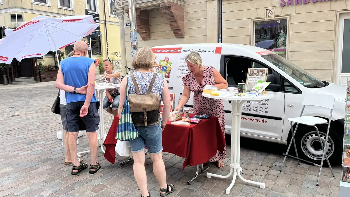 das Auto der Verbraucherzentrale mit einem Infostand davor, vor dem stand stehen Menschen