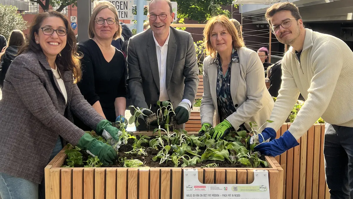 Verschiedene Personen stehen um ein Hochbeet und pflanzen gemeinsam.