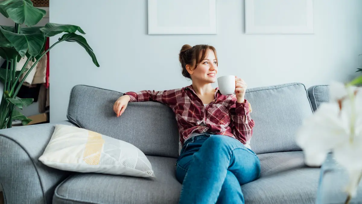 Eine Frau sitz entspannt mit einer Tasse in der Hand auf dem Sofa