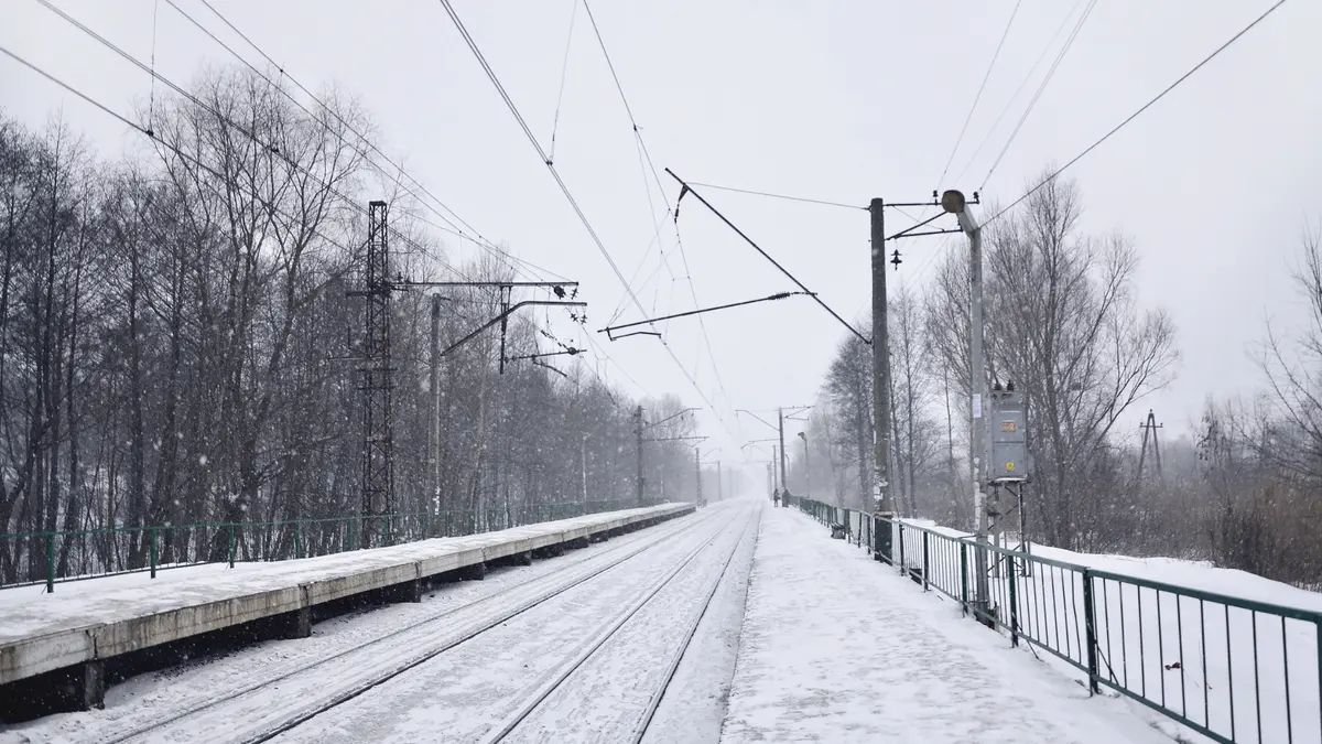Eine eingeschneite Bahnstrecke mit Oberleitungen und Bäumen