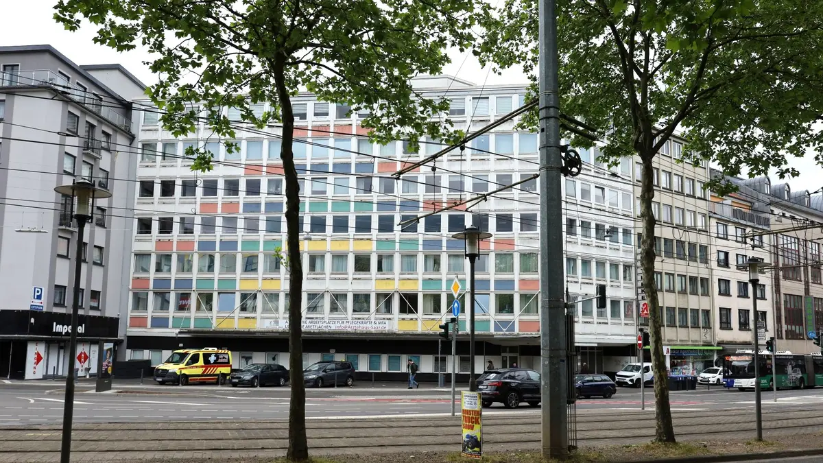 Ansicht eines mehrstöckigen Gebäudes mit farbiger Gestaltung der Frontseite, Straße mit Straßenbahngleisen, ein parkender Krankenwagen