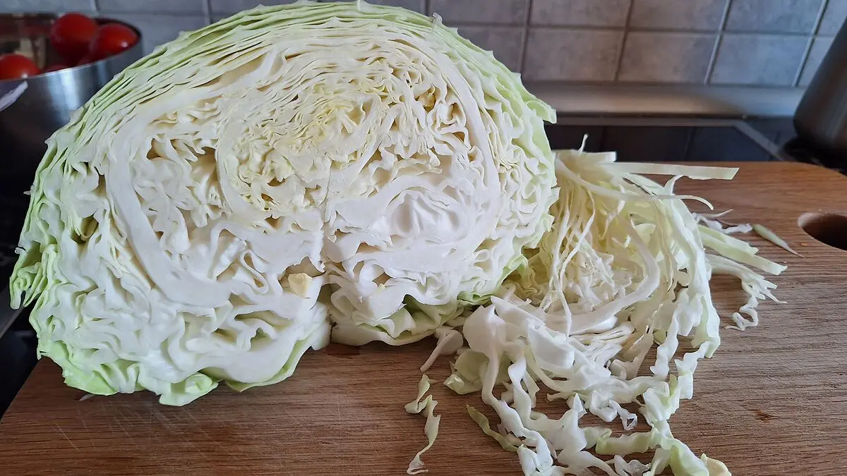 Ein halber Jaroma-Kohl liegt auf einem Holzbrett, daneben befinden sich fein geschnittene Kohlstreifen.