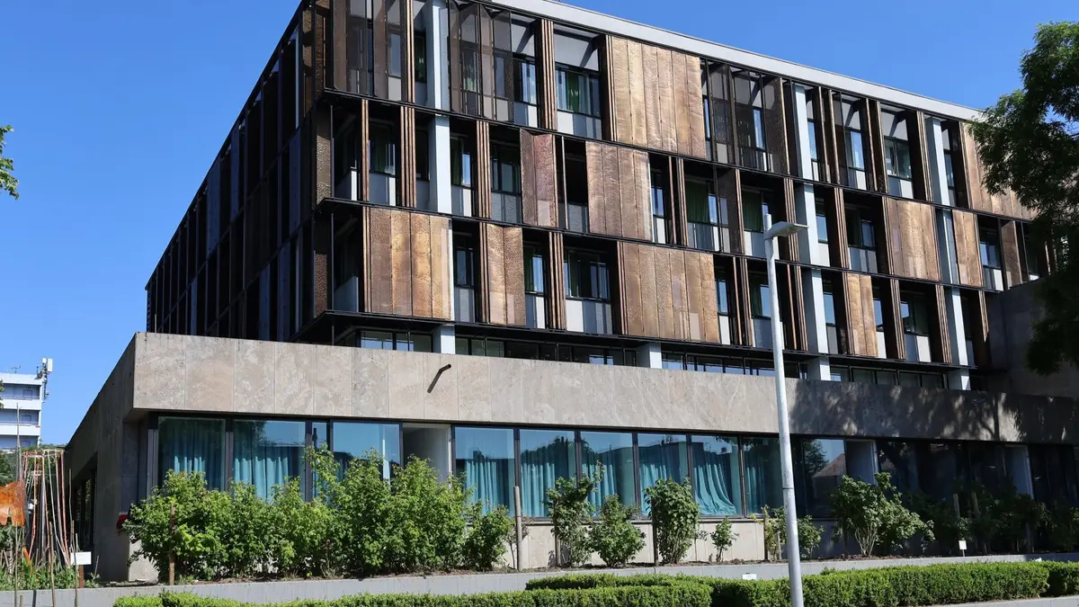 Mehrstöckiges Gebäude vor blauem Himmel, im Vordergrund viele grüne Pflanzen, Design-Verblendung des Hauses aus oxidiertem Corten-Stahl