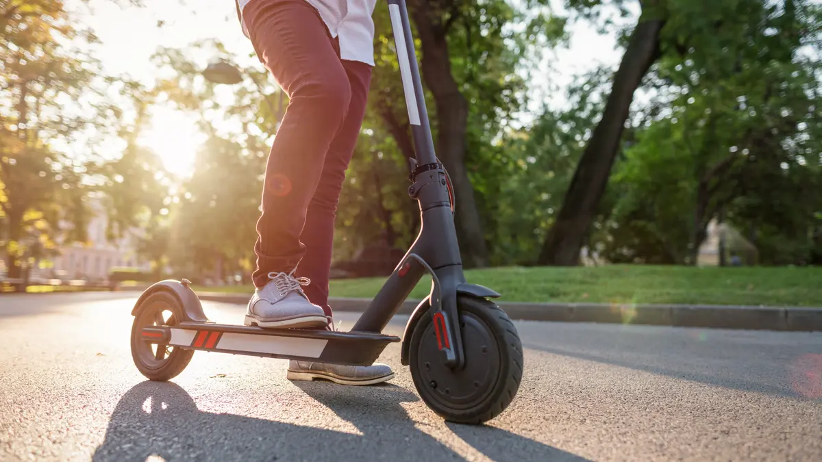 Eine Person steht mit auf einem E-Scooter im Park.