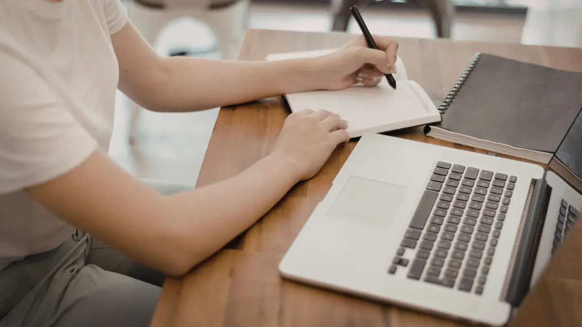 Person sitzt am Laptop und macht Notizen
