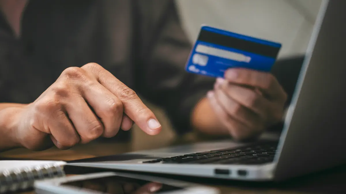 eine Person hält eine Kreditkarte in der Hand während sie vor einem Laptop sitzt