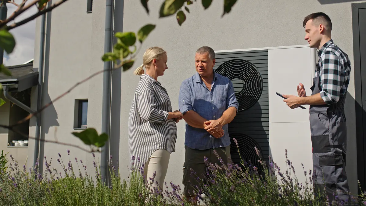 Energieberater mit einem Paar in einer Energieberatung an einer Wärmepumpe vor einem Wohnhaus