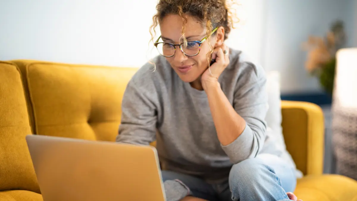 Eine Frau sitzt auf einem gelben Sofa vor einem Laptop