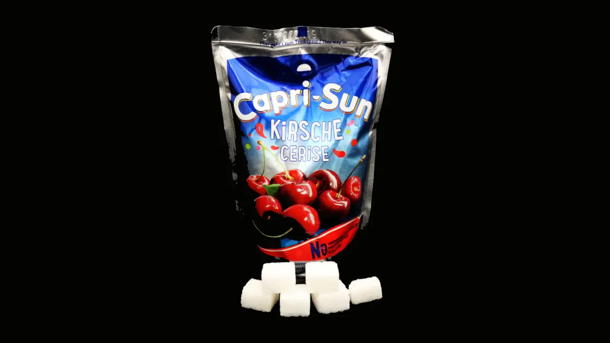 Packung Capri Sonne Kirsche auf schwarzem Grund mit 5,5 Zuckerwürfeln davor