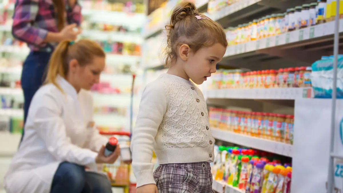Ein Mädchen steht im Drogeriemarkt vor einem Regal mit Quetschies und anderen Kindersnacks