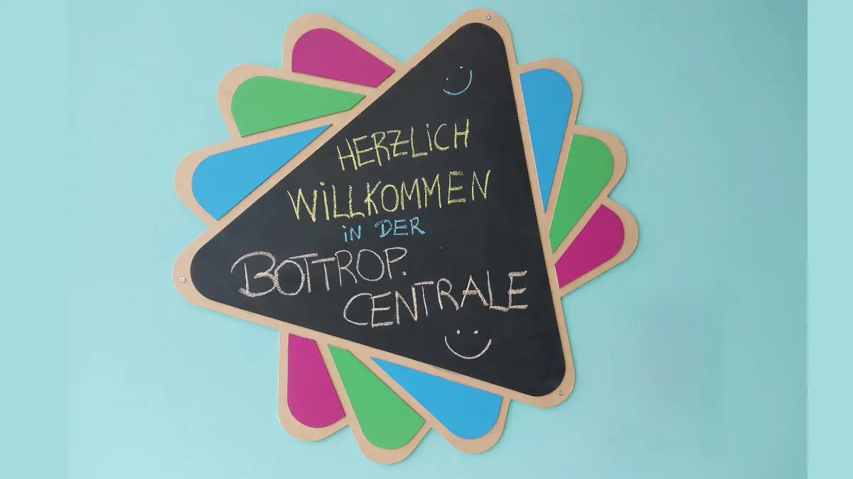 Kreidetafel in Form eines Dreiecks, auf der handschriftlich geschrieben steht: "Herzlich willkommen in der Bottrop.Centrale"