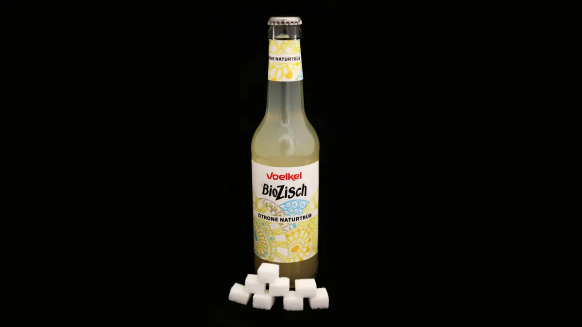 Flasche Biozisch Zitrone auf schwarzem Grund mit 8 Zuckerwürfeln davor