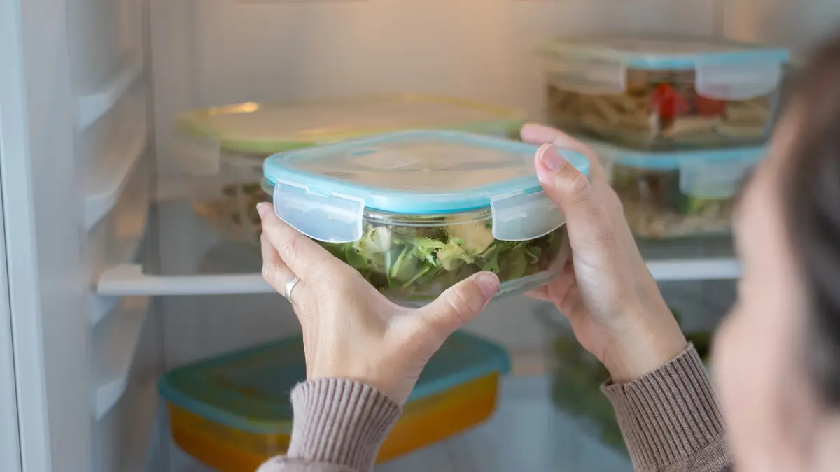 Eine Frau räumt Salat in einer Kühlbox in den Kühlschrank.