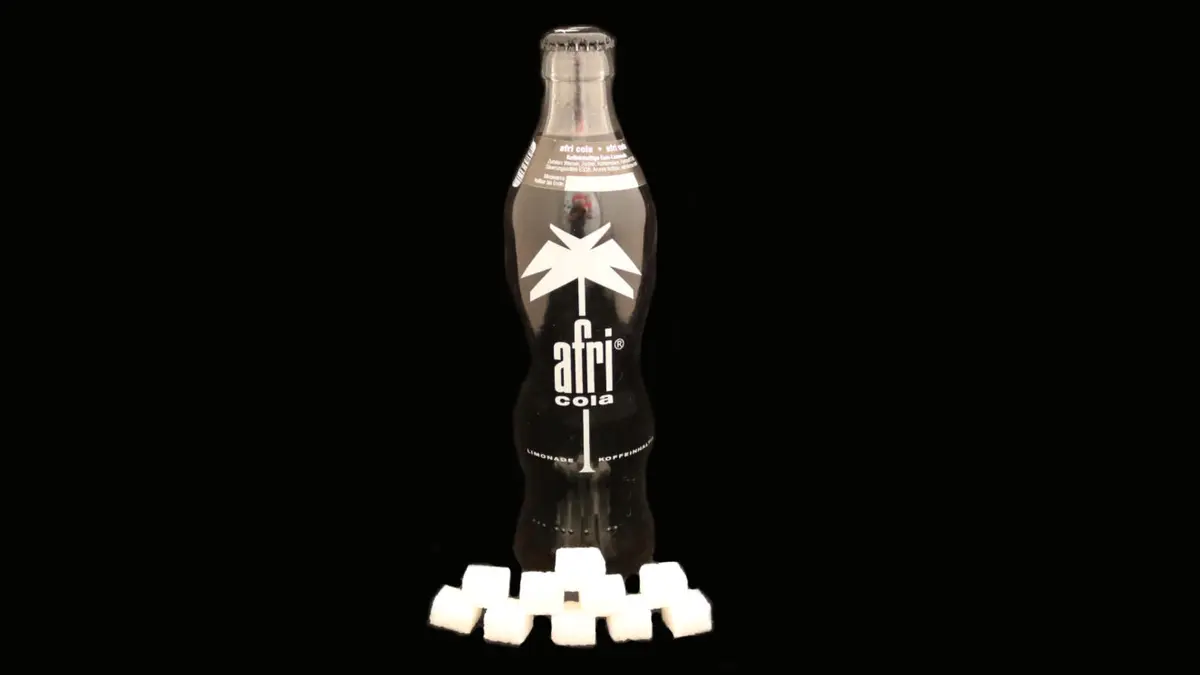 Flasche Afri Cola auf schwarzem Grund mit 10 Zuckerwürfeln davor