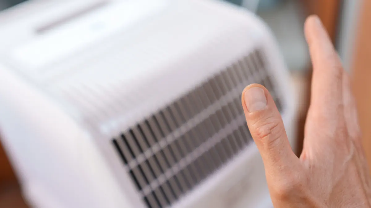 Ein Mann hält seine Hand zum Abkühlen an eine mobile Klimaanlage