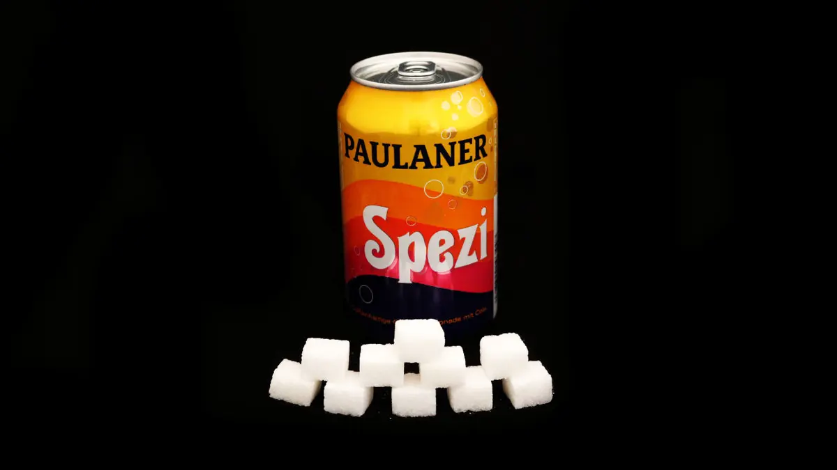 Dose Paulaner Spezi auf schwarzem Grund mit 10 Zuckerwürfeln davor