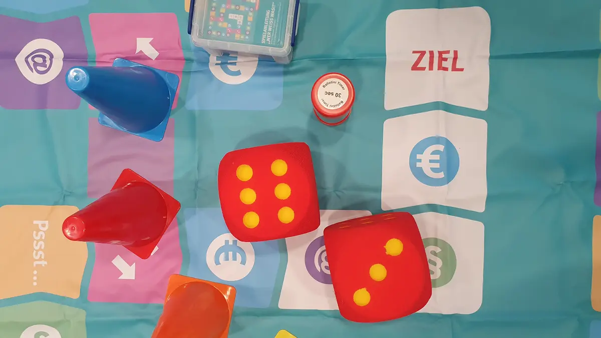 Verschiedenfarbige Spielfiguren und zwei Würfel, auf einem Spielfeld liegend