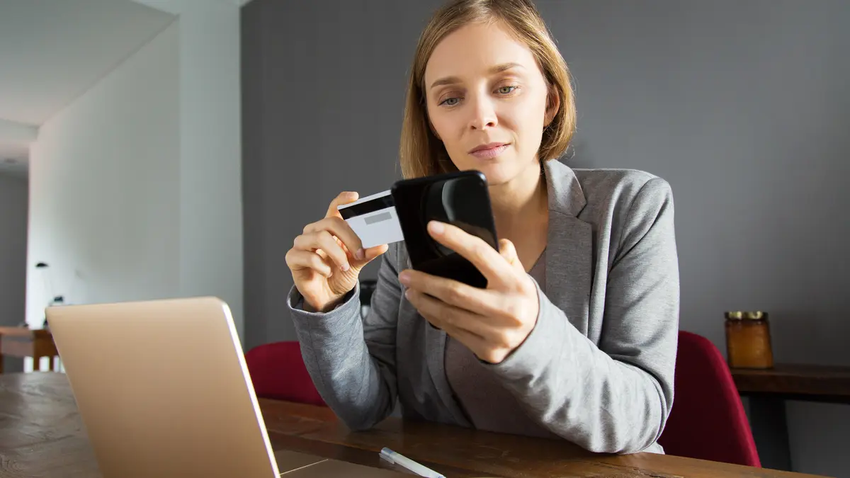 Eine junge Frau bezahlt etwas am Smartphone mit ihrer Bankkarte 