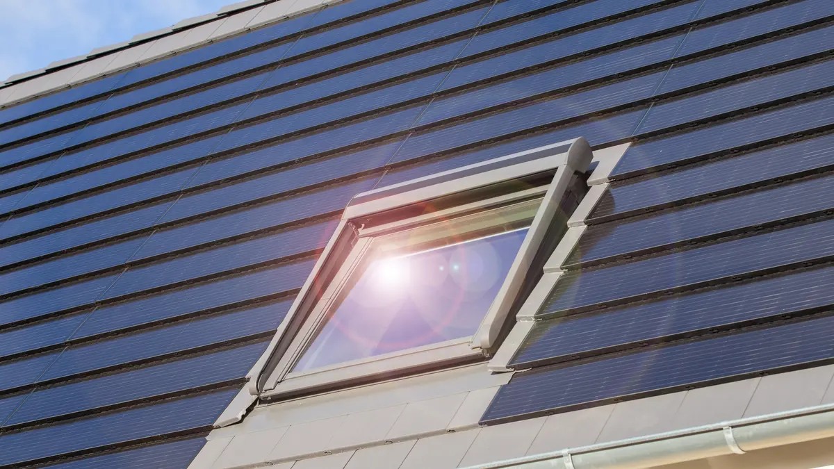 Solardachziegel umgeben ein Dachfenster, das das Sonnenlicht reflektiert.