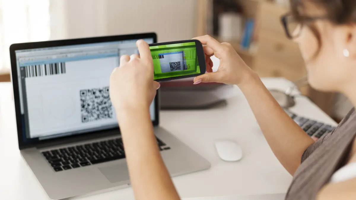 Eine Frau scannt mit ihrem Handy einen QR-Code am Laptop, um zu bezahlen