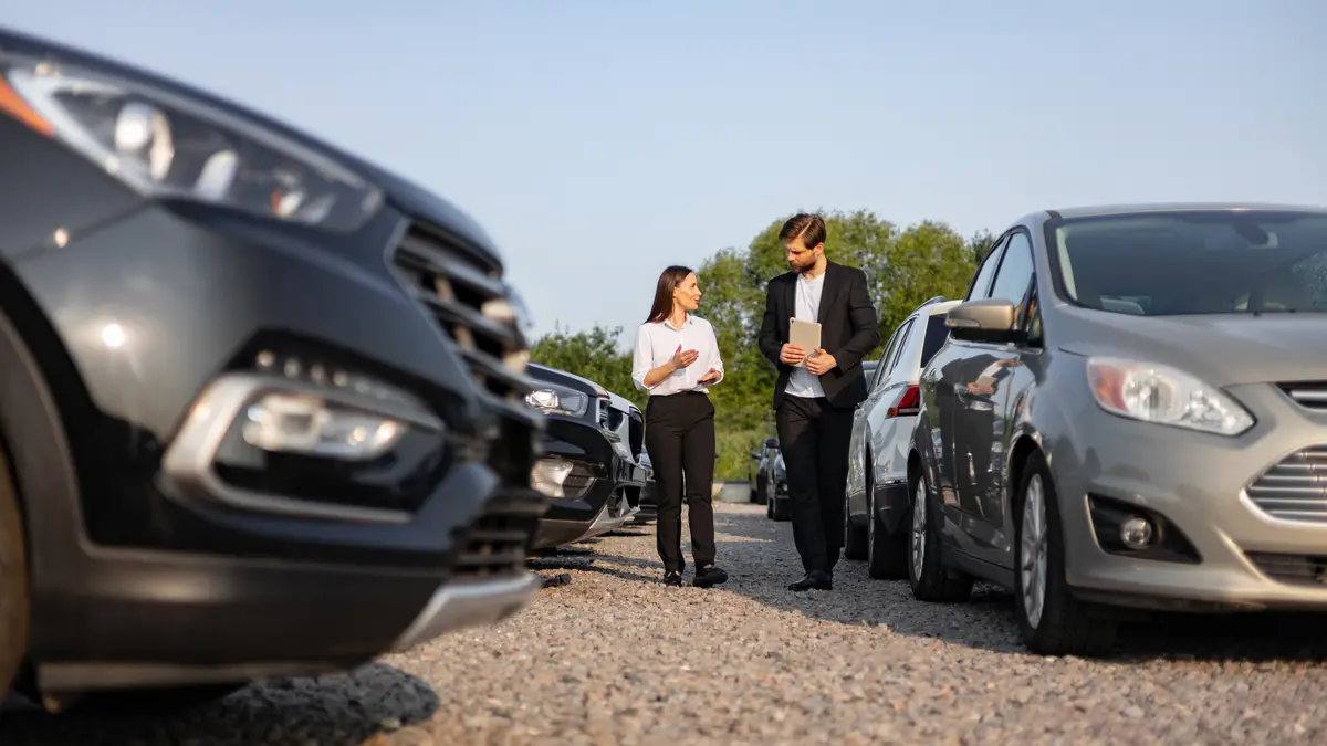 Frau und Gebrauchtwagenhändler zwischen Autos, die zum Verkauf stehen. Sonniges Wetter.