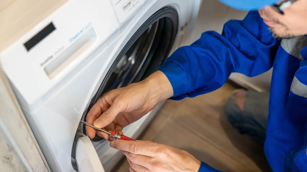 Ein Techniker repariert die Türdichtung einer Waschmaschine mit einem Schraubendreher.