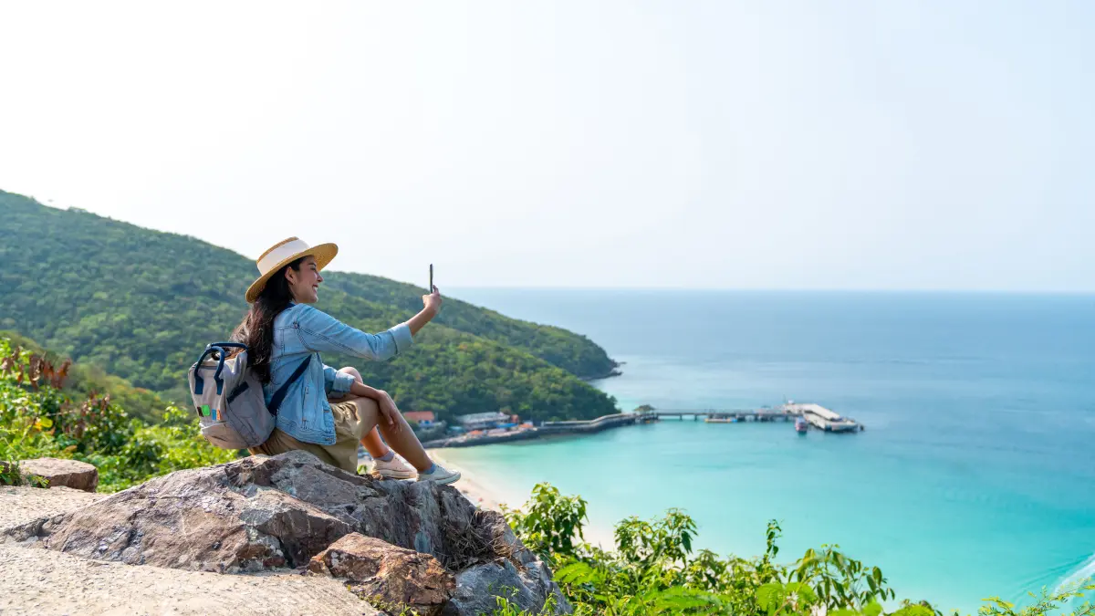 Frau nutzt Mobiltelefon im Urlaub auf Insel mit Berg