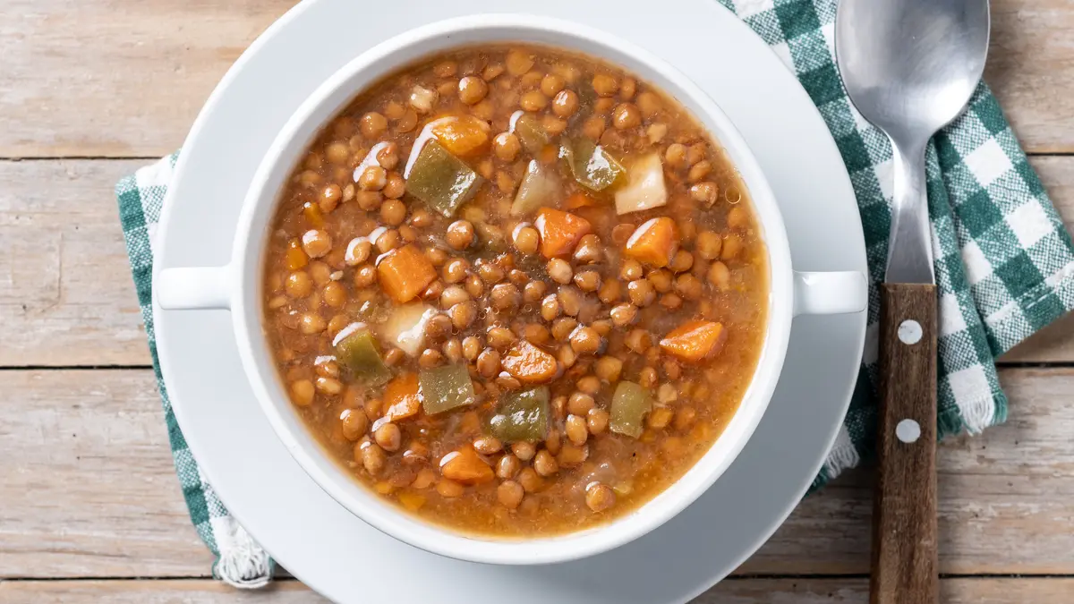 Ein Teller mit Linsensuppe, rechts davon ein Esslöffel auf einer grün-weiß karierten Serviette