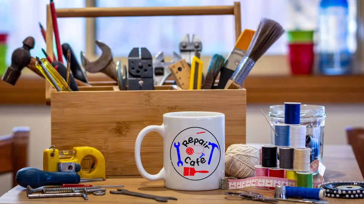 Ein Werkzeugkasten steht neben Näh-Utensilien und einem Kaffeebecher mit der Aufschrift "Repair-Café".