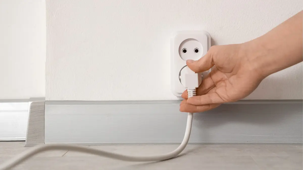 Frauenhand zeiht Stecker aus Steckdose an heller Wand