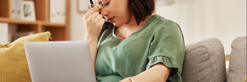 Frau auf dem Sofa mit Laptop auf dem Schoß mit frustriertem Gesichtsausdruck